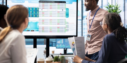 Réunion d’équipe analysant des tableaux de données sur écran dans le cadre d’un projet d’automatisation appels d'offres.