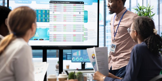 Réunion d’équipe analysant des tableaux de données sur écran dans le cadre d’un projet d’automatisation appels d'offres.