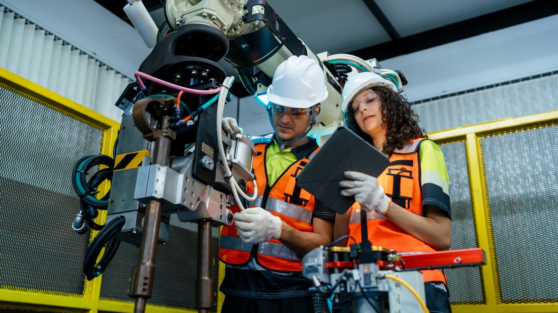 Two technicians in safety equipment programme a fixed robotic arm designed to interact with the factory’s autonomous mobile robot (AMR) fleet.