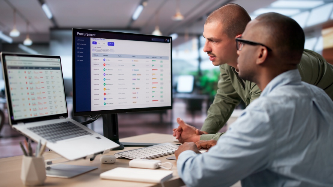 Two colleagues reviewing purchase orders together on a large screen, using their guided buying portal to optimise procurement.