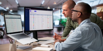 Two colleagues reviewing purchase orders together on a large screen, using their guided buying portal to optimise procurement.