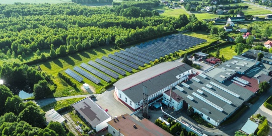 An aerial view of an industrial facility with a vast field of solar panels, demonstrating a renewable energy production approach as part of a regenerative economy.