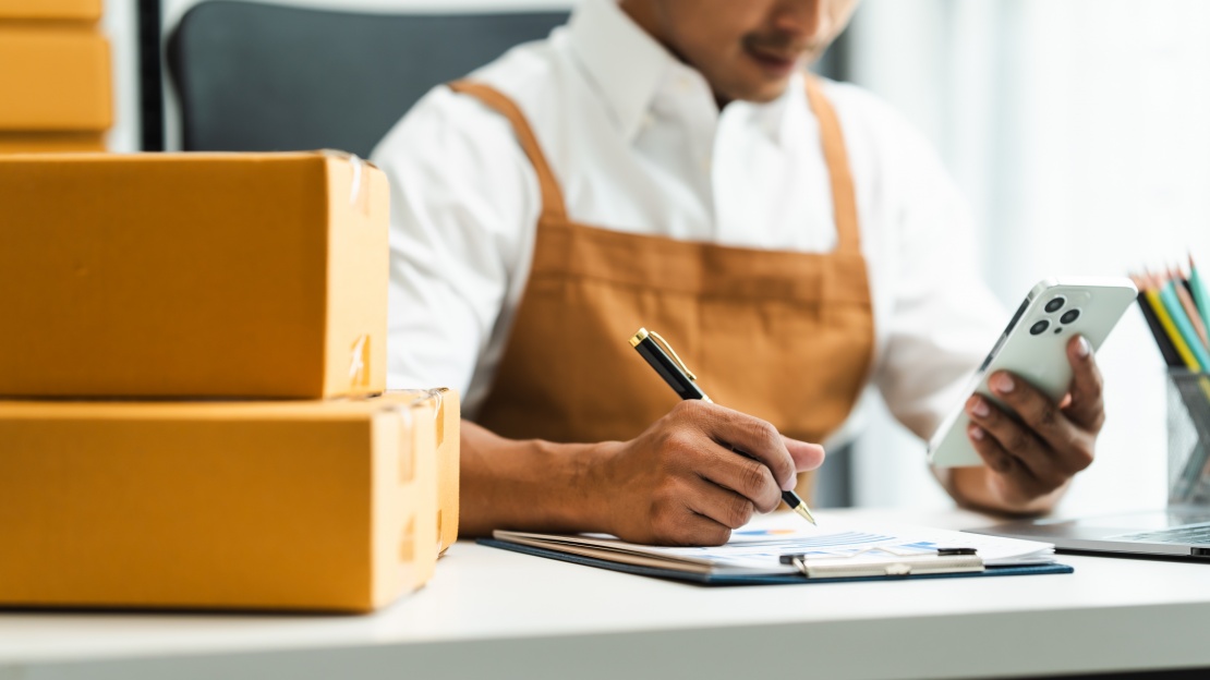 A purchasing manager validates information on a clipboard while consulting their smartphone, demonstrating the efficiency of mobile procurement for stock management.