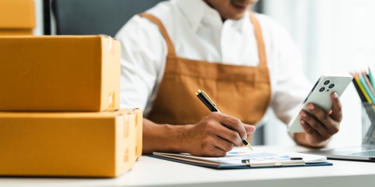 A purchasing manager validates information on a clipboard while consulting their smartphone, demonstrating the efficiency of mobile procurement for stock management.