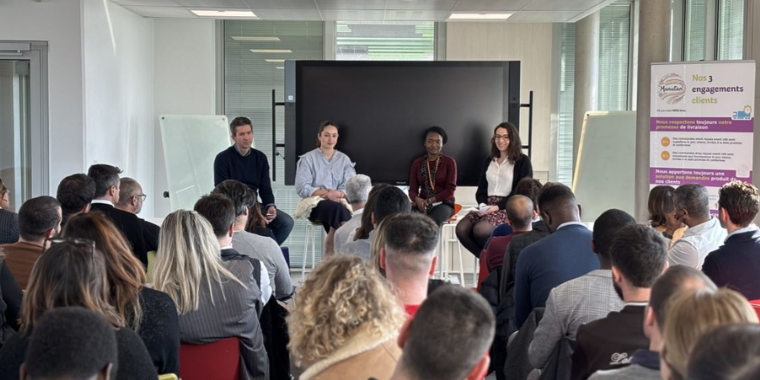 In-company conference with four speakers seated on stools in front of an attentive audience. 