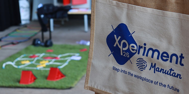 Sac en toile aux couleurs de Xperiment Manutan devant un espace d’animation illustrant les environnements de travail et solutions innovantes présentés lors de l’événement