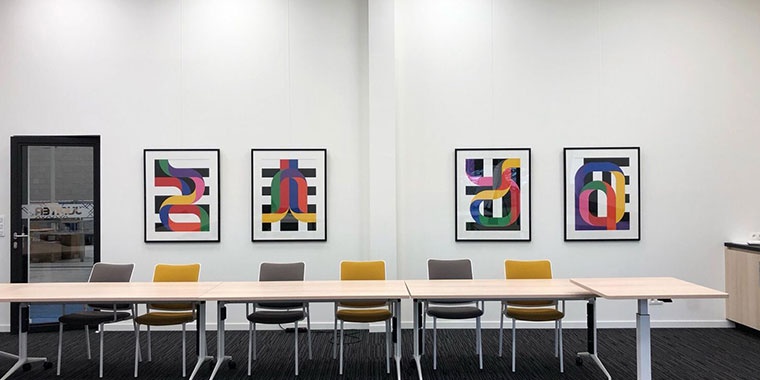 Photo of a room with four paintings on the wall facing a large table with six chairs.